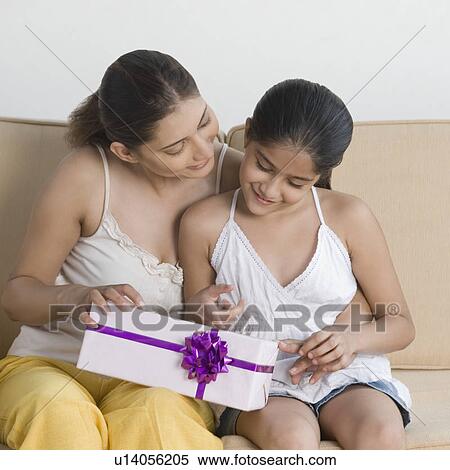 Stock Photography - Close-up of a young woman sitting on a couch with her daughter and holding a gift. Fotosearch