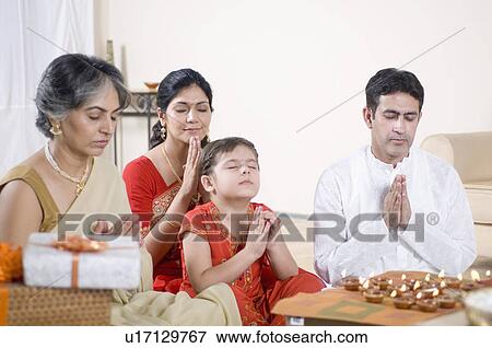 Stock Photo - Family praying in front of figurines of God. Fotosearch