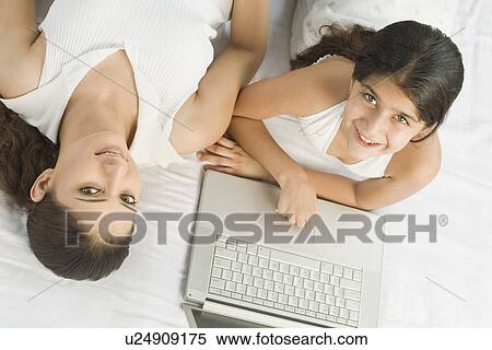 High angle view of a girl using a laptop on the bed beside her mother View Large Photo Image Stock Photography - High angle view of a girl using a laptop on the bed beside her mother. Fotosearch