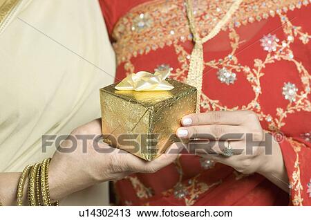 Stock Image - Mid section view of two women holding a gift. Fotosearch