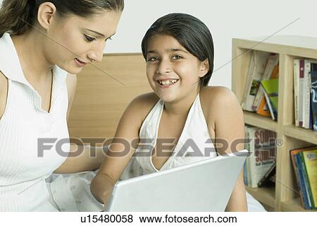 Stock Photo - Portrait of a girl sitting in front of a laptop with her mother and smiling. Fotosearch
