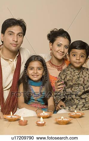 Stock Image - Portrait of a young couple sitting together with their son and daughter behind diwali lamps. Fotosearch