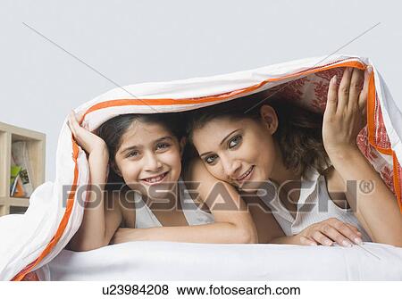 Portrait of a young woman lying on the bed with her daughter under a blanket and smiling View Large Photo Image Stock Photo - Portrait of a young woman lying on the bed with her daughter under a blanket and smiling. Fotosearch