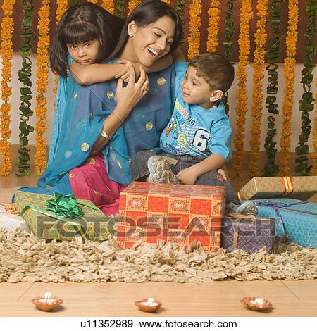 Young woman with her two children sitting behind diwali gifts and smiling View Large Photo Image Stock Photo - Young woman with her two children sitting behind diwali gifts and smiling. Fotosearch