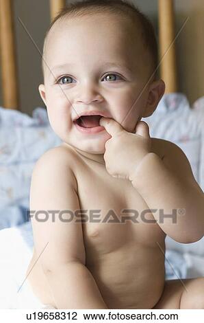 Stock Image - Close-up of a baby boy sitting in a crib and putting his finger in his mouth. Fotosearch