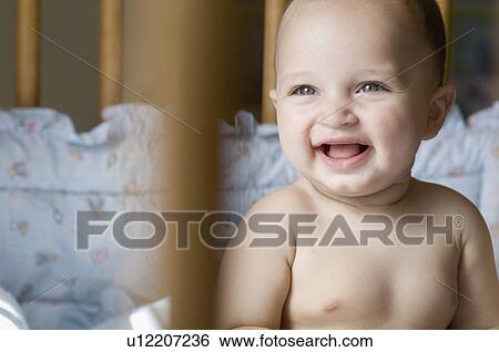 Stock Photograph - Close-up of a baby boy sitting in a crib and smiling. Fotosearch