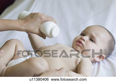 Stock Photograph - Close-up of a person's hand putting talcum powder on the chest of a baby. Fotosearch