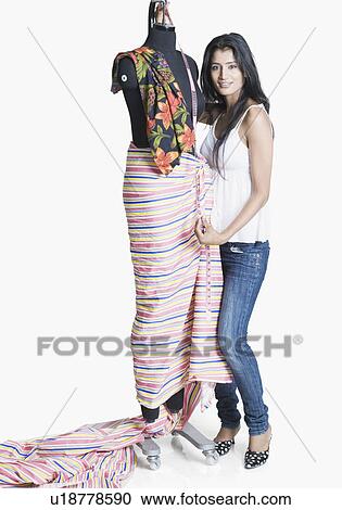 Stock Image - Portrait of a female fashion designer measuring the length of a mannequin with a tape measure. Fotosearch