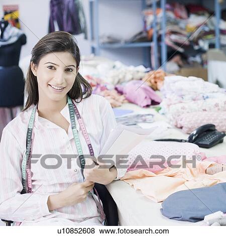 Stock Photo - Portrait of a female fashion designer sitting in a textile industry and smiling. Fotosearch