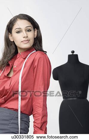 Portrait of a female fashion designer standing in front of a mannequin View Large Photo Image Stock Photography - Portrait of a female fashion designer standing in front of a mannequin. Fotosearch