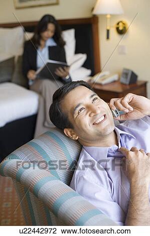Businessman talking on a mobile phone and smiling with a businesswoman reading a file in the background View Large Photo Image Stock Image - Businessman talking on a mobile phone and smiling with a businesswoman reading a file in the background. Fotosearch