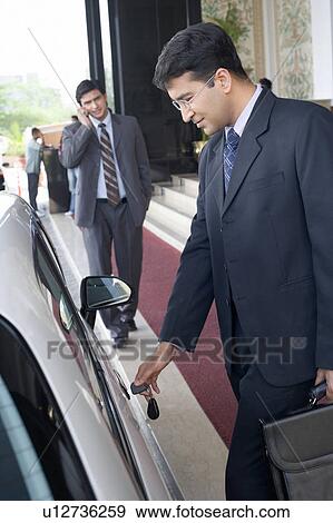 Businessman unlocking his car with another businessman talking on a mobile phone in the background View Large Photo Image Stock Photo - Businessman unlocking his car with another businessman talking on a mobile phone in the background. Fotosearch