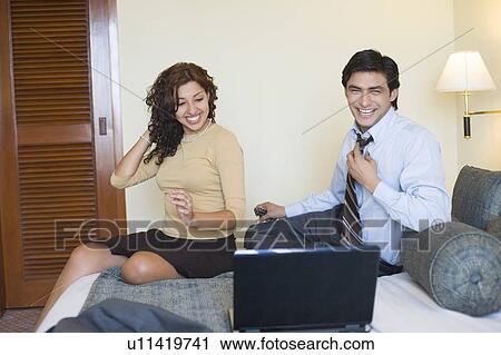 Businessman with a young woman sitting on the bed and looking at a laptop View Large Photo Image Stock Image - Businessman with a young woman sitting on the bed and looking at a laptop. Fotosearch