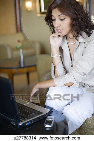 Picture - Businesswoman looking at a laptop with her hand on her chin. Fotosearch