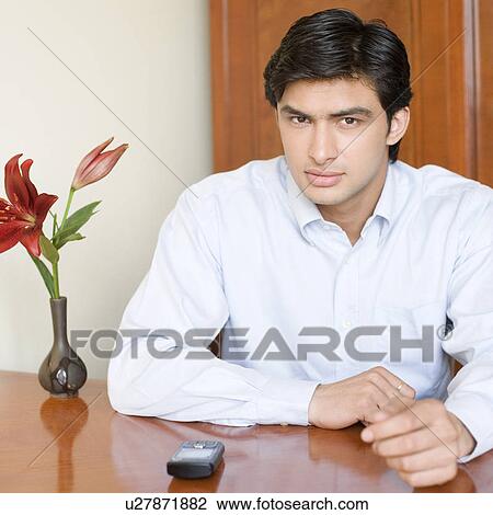 Portrait of a young man sitting at a table View Large Photo Image Stock Image - Portrait of a young man sitting at a table. Fotosearch