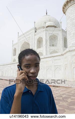 Stock Image - Portrait of a young man talking on a mobile phone in front of mausoleum, Taj Mahal, Agra, Uttar Pradesh, India. Fotosearch