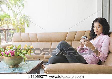 Side profile of a young woman sitting on a couch and operating a mobile phone View Large Photo Image Stock Photo - Side profile of a young woman sitting on a couch and operating a mobile phone. Fotosearch