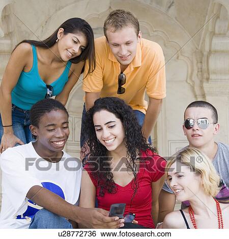 Stock Photograph - Three young couples looking at a mobile phone and smiling, Taj Mahal, Agra, Uttar Pradesh, India. Fotosearch