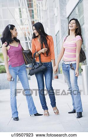 Stock Image - Three young women carrying their hand bags and smiling. Fotosearch