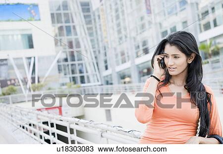 Stock Image - Young woman leaning against a railing and talking on a mobile phone. Fotosearch