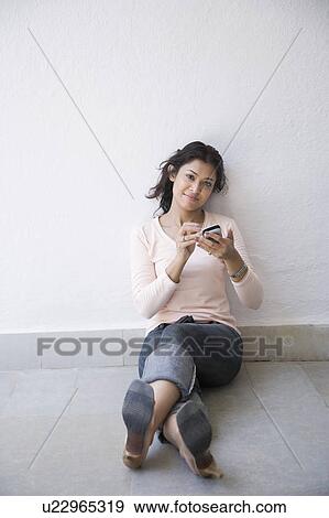 Young woman leaning against a wall and operating a mobile phone View Large Photo Image Stock Photo - Young woman leaning against a wall and operating a mobile phone. Fotosearch