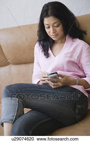 Young woman sitting on a couch and operating a mobile phone View Large Photo Image Stock Image - Young woman sitting on a couch and operating a mobile phone. Fotosearch