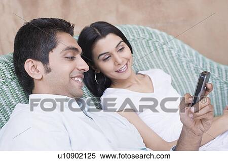 Close-up of a young couple looking at a mobile phone and smiling View Large Photo Image Stock Photography - Close-up of a young couple looking at a mobile phone and smiling. Fotosearch