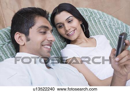 Close-up of a young man holding a mobile phone with a young woman sitting beside him View Large Photo Image Stock Image - Close-up of a young man holding a mobile phone with a young woman sitting beside him. Fotosearch
