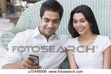 Close-up of a young man holding a mobile phone with a young woman sitting beside him View Large Photo Image Stock Photograph - Close-up of a young man holding a mobile phone with a young woman sitting beside him. Fotosearch