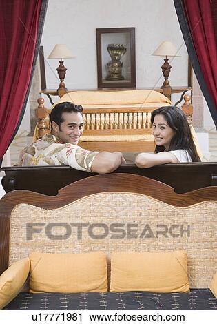 Stock Image - Portrait of a young couple sitting on a couch and smiling. Fotosearch