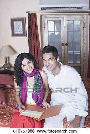 Portrait of a young couple sitting on the bed and smiling View Large Photo Image Stock Photograph - Portrait of a young couple sitting on the bed and smiling. Fotosearch