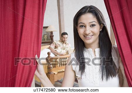 Portrait of a young woman holding curtains with a young man lying in the background View Large Photo Image Stock Image - Portrait of a young woman holding curtains with a young man lying in the background. Fotosearch