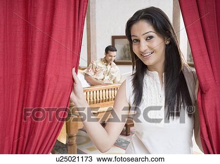 Portrait of a young woman holding curtains with a young man lying in the background View Large Photo Image Stock Image - Portrait of a young woman holding curtains with a young man lying in the background. Fotosearch