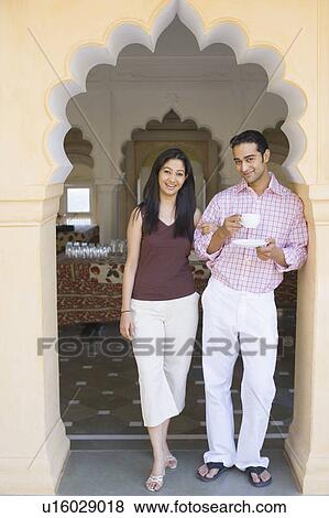 Portrait of a young woman standing arm in arm with a young man holding a cup of tea View Large Photo Image Stock Photo - Portrait of a young woman standing arm in arm with a young man holding a cup of tea. Fotosearch