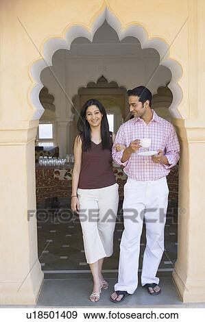 Stock Photo - Portrait of a young woman standing arm in arm with a young man holding a cup of tea and saucer. Fotosearch