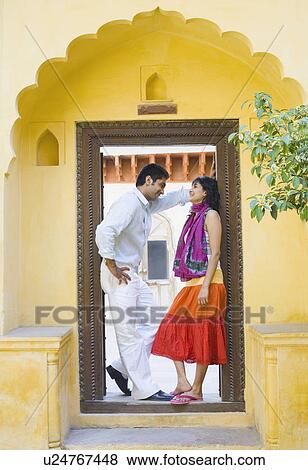 Stock Photo - Side profile of a young couple standing at the entrance of a house and smiling. Fotosearch
