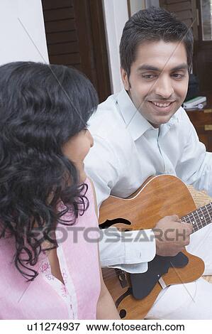 Side profile of a young man sitting with a young woman and playing a guitar View Large Photo Image Stock Photo - Side profile of a young man sitting with a young woman and playing a guitar. Fotosearch