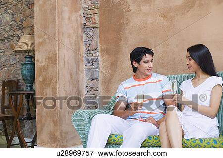 Young couple sitting on a couch and holding champagne flutes View Large Photo Image Stock Photo - Young couple sitting on a couch and holding champagne flutes. Fotosearch