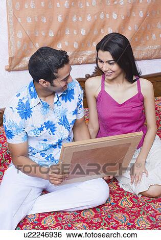 Stock Photograph - Young couple sitting on the bed and holding a picture frame. Fotosearch