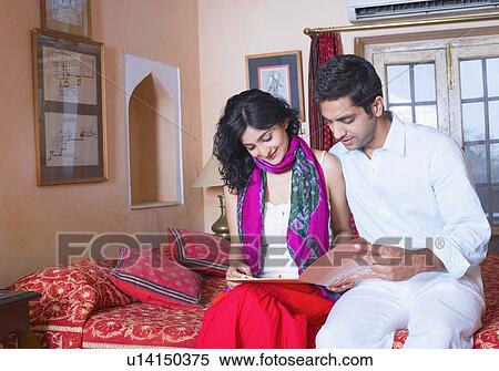 Stock Photography - Young couple sitting on the bed and looking at a file. Fotosearch