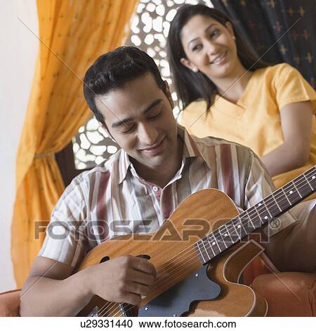 Young man playing a guitar with a young woman sitting behind him View Large Photo Image Stock Image - Young man playing a guitar with a young woman sitting behind him. Fotosearch