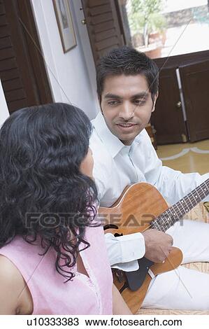 Young man playing the guitar with a young woman beside him View Large Photo Image Stock Image - Young man playing the guitar with a young woman beside him. Fotosearch
