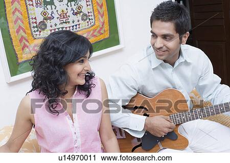 Young man playing the guitar with a young woman sitting beside him View Large Photo Image Stock Image - Young man playing the guitar with a young woman sitting beside him. Fotosearch