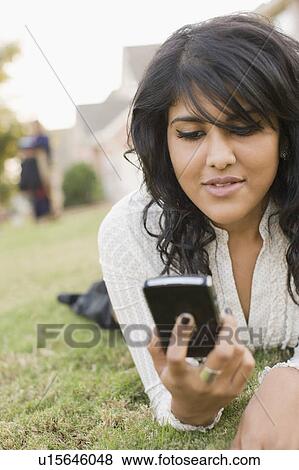 Stock Photo - Close-up of a young woman lying on the grass and looking at a mobile phone. Fotosearch