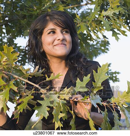 Close-up of a young woman standing near a tree and smirking View Large Photo Image Stock Photo - Close-up of a young woman standing near a tree and smirking. Fotosearch