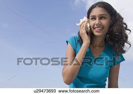 Low angle view of a young woman holding a conch shell to her ear and smiling View Large Photo Image Stock Image - Low angle view of a young woman holding a conch shell to her ear and smiling. Fotosearch