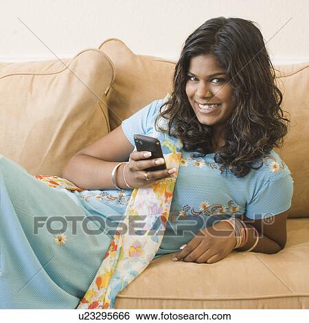 Stock Photograph - Portrait of a young woman holding a mobile phone on a couch. Fotosearch