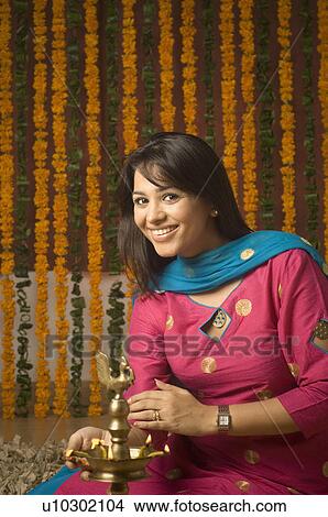 Picture - Portrait of a young woman lighting a diwali lamp and smiling. Fotosearch