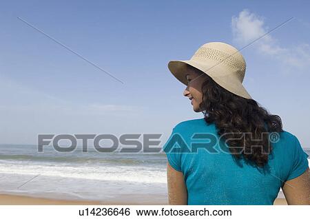 Stock Photograph - Rear view of a young woman standing on the beach. Fotosearch
