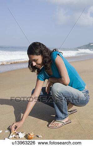 Side profile of a young woman playing with seashells on the beach View Large Photo Image Stock Photograph - Side profile of a young woman playing with seashells on the beach. Fotosearch